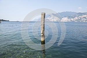 Wooden bricole for boats in the water, lake Lago Di Garda, morning light, mountains on the background photo