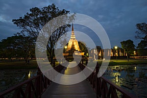 The wooden bridge conducting to ruins of the ancient Buddhist temple of Wat Sa Si in evening twilight. Sukhothai, Thailand
