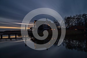 Wooden bridge leading to a cottage over a lake captured at night