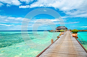 Wooden bridge leading to an exotic bungalow on the background of azure water, maldives