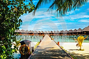 Wooden bridge leading to an exotic bungalow on the background of azure water, maldives