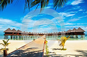 Wooden bridge leading to an exotic bungalow on the background of azure water, maldives