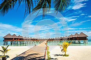 Wooden bridge leading to an exotic bungalow on the background of azure water, maldives