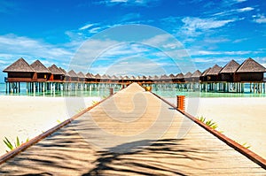 Wooden bridge leading to an exotic bungalow on the background of azure water, maldives