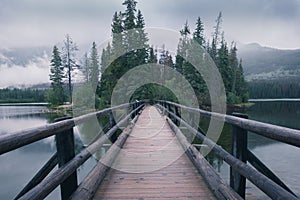 Wooden bridge leading to a small island in the background. Pyramid Lake in Canadian Rockies. Misty, rainy evening in Jasper