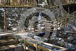 Wooden bridge over a small stream in the forest. Waterfall in the garden with rocks and leaves in autumn season.