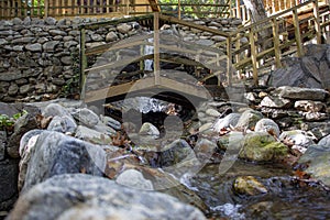 Wooden bridge over a small stream in the forest. Waterfall in the garden with rocks and leaves in autumn season.