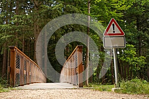 A wooden bridge in the park and a road danger sign.