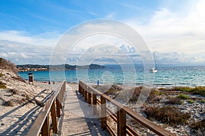 A wooden bridge leads to a sandy beach on the island of Sardinia in Italy. Beautiful sea with a small boat in the Costa Smeralda.