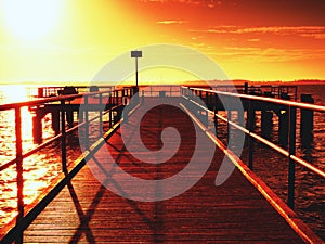 Wooden bridge at the sea at sunset. Windless weather, peaceful silent day in bay.