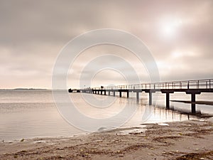 Wooden bridge at the sea at sunset. Windless weather, peaceful silent day in bay.