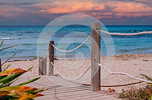 Wooden bridge to the beach and ocean at menorca spain with sunset