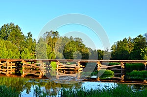 A wooden bridge of tree logs lies across a small river inside a wooded area among green nature