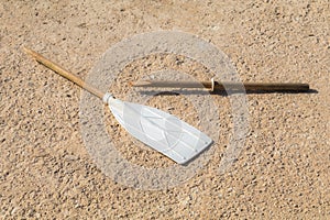 Wooden broken oar, on tan concrete, in the sun.