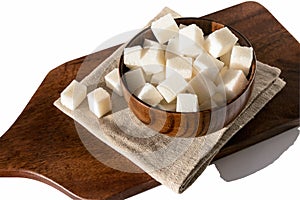 In a wooden brown bowl, white lumpy beet sugar in the form of a cube on a linen napkin.