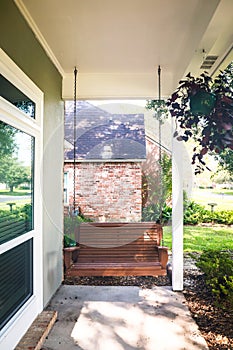 A wooden brown outdoor porch swing on a small front porch of a house