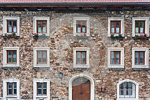 A wooden, brown windows and a fragment of a stone wall of the building. Curtains hanging in the window, colorful flowers