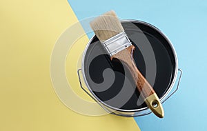 Wooden brush on black color paint can on blue and yellow background with copy space