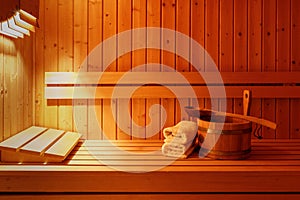 Wooden bucket with spoon, white towels on bench in sauna interior