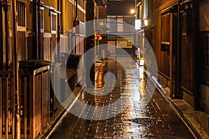 Wooden buildings line wet alley in historic Kyoto district