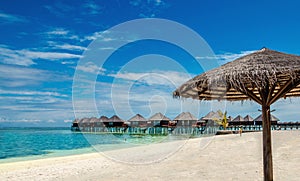 Wooden bungalow and palm tree umbrella on the background of azure water and blue sky, Maldives