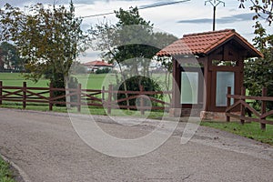Wooden bus station in the village. Empty rural bus station along road with fence and trees. Travel and destination concept.