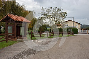 Wooden bus station in the village. Empty rural bus station along road with fence and trees. Travel and destination concept.