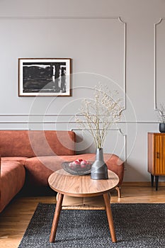 Wooden cabinet with black vases in the corner of classy grey living room interior with ginger sofa