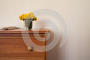 Wooden cabinet with vase of yellow flowers and piece of white material.