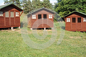 Wooden cabins or lodges as summerhouses in a forest with green grass on a sunny summer day