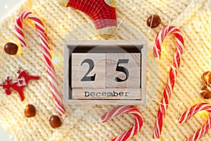 Wooden calendar blocks with Christmas candy cane, garlands and Christmas decorations on knitted white background. December 25th da