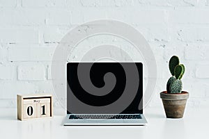 Wooden calendar with date of 1st may, laptop with blank screen and cactus plant