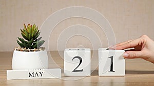 Wooden calendar with an important event for May 21, a woman`s hand sets the date on the calendar. Spring season.