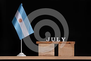 Wooden calendar of Jule with Argentine flag on black background. Holidays of Argentina in Jule