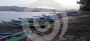 Wooden canoes of various colors lined the shore. with a backdrop of hills and plumes of smoke