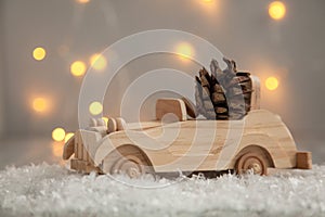 Wooden car with pine cone on a wooden gray background and lights from the garland. Christmas concept