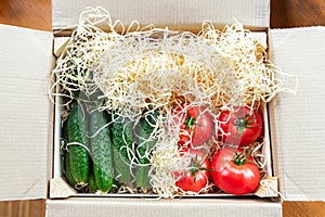 Wooden and cardboard crate box with fresh ripe tasty red tomatoes and green cucumbers with wood shavings filler