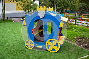 A wooden carriage of bright blue and yellow color against a background of green trees and residential buildings
