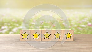 Wooden cartoon cube five yellow star review on blur field of flowers background. Service rating, satisfaction concept. reviews and