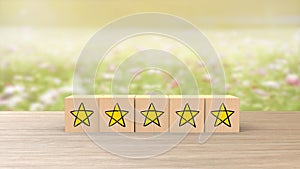 Wooden cartoon cube five yellow star review on blur field of flowers background. Service rating, satisfaction concept. reviews and