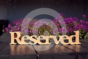 Wooden carved reserved table sign , pink flowers background, wooden table in outdoor restaurant