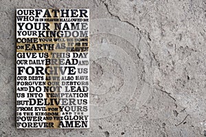 Wooden carved word of the Lord`s Prayer on the grey concrete background.