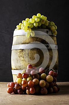 wooden cask with wine and two grapes on a black background