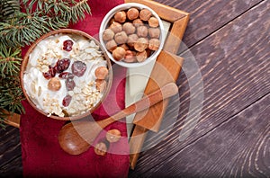 Wooden and ceramic bowls of yogurt and hazelnuts on red napkin on tray on wooden table.