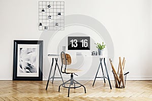 Wooden chair at desk with desktop computer in white home office interior with poster. Real photo
