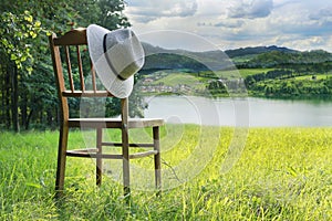 Wooden chair and a hat in the garden with view on lake  hills and mountains in the distance