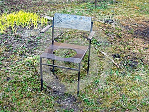 A wooden chair, a hole in the middle of the chair to fit a toilet, an old object