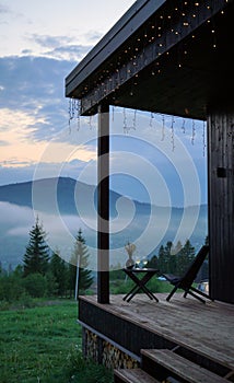 wooden chair and table on cabin terrace with foggy mountain view evening in blue hour