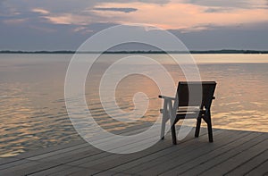 Wooden chair on a wood pier overlooking calm lake at sunset skyline