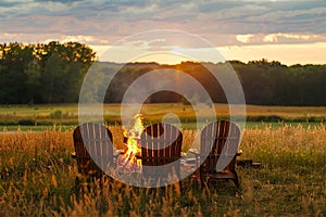 Wooden chairs near the bonfire in summer meadow, sunset